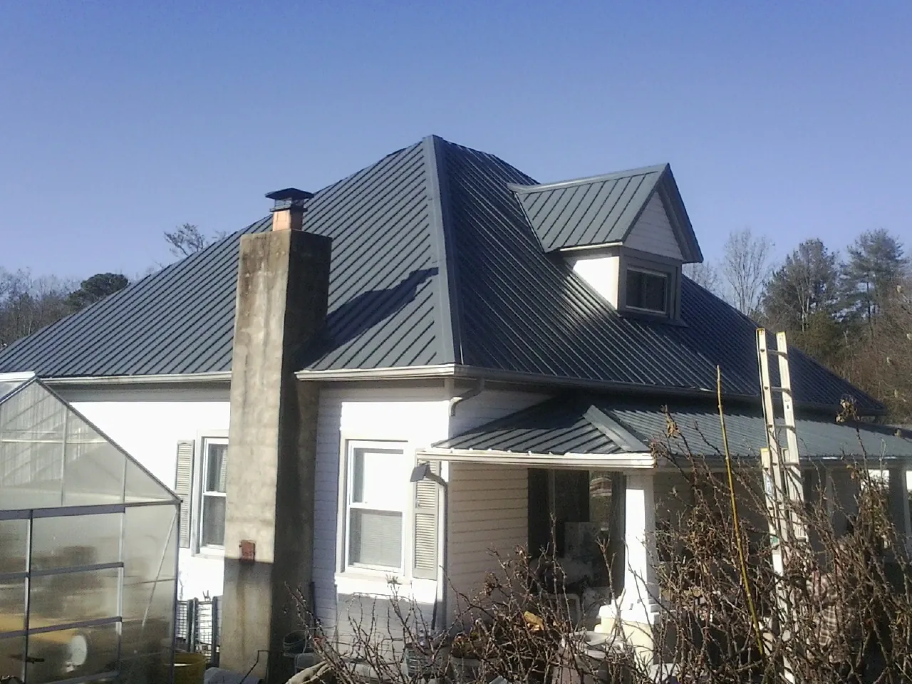 Dark blue standing seam metal roof on a white farmhouse with dormer — Slate & Tile Roof Repair by Roofing Brothers in Rangely