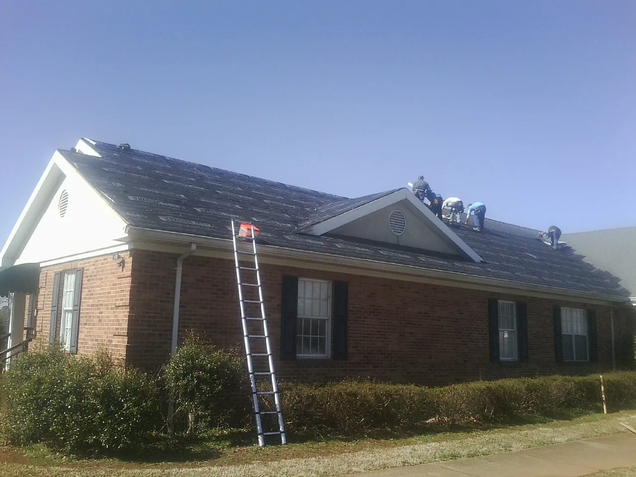 Crew tearing shingles off a brick ranch roof with a ladder set — Emergency Roof Repair work by our crew in Rangely