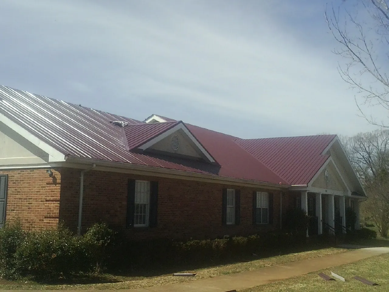 Red metal roof with gabled entries on a long brick building, from a Hail Damage Roof Repair job in Rangely