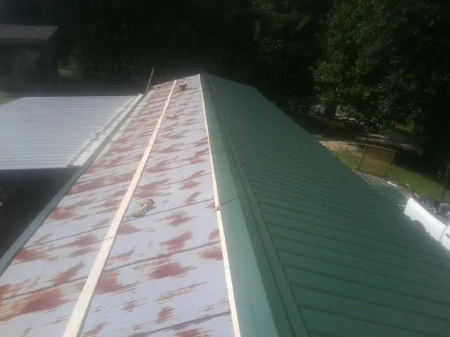 Old rusted panels beside newly installed green metal roofing — Wind Damage Roof Repair by Roofing Brothers in Rangely